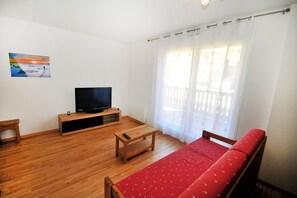 A room with a wooden floor, a TV on a stand, a red sofa, and a painting on the wall. - Mountain apartment at the start of cross-country skiing and hiking trails (Villar-d'Arêne)