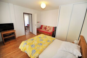 A bedroom with a bed, a TV on a stand, a wardrobe, and a door leading to another room. - Mountain apartment at the start of cross-country skiing and hiking trails (Villar-d'Arêne)