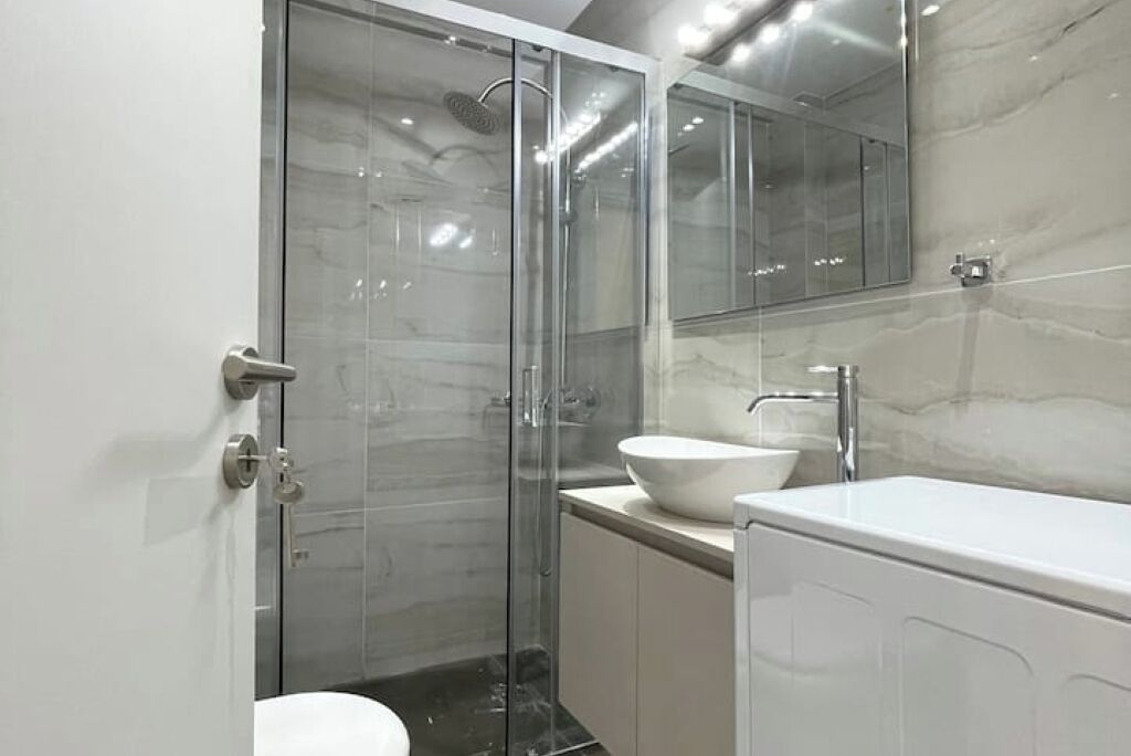 A modern bathroom with a glass-enclosed shower, a white sink, and a large mirror.