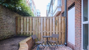 A patio with a brick floor, a wooden fence, and two metal chairs. - The Abbey Mews House (London)