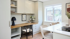 A modern kitchen with white cabinetry, a wooden countertop, a dining area with chairs, and a window with a view. - The Abbey Mews House (London)