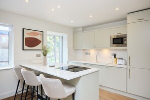 Een moderne keuken met een centraal eiland, barstoelen, witte kastjes en een magnetron.