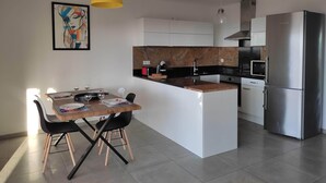 Een moderne keuken met een centraal eiland, roestvrijstalen apparatuur en een eethoek met een houten tafel en zwarte stoelen.