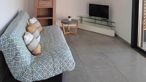 Een woonkamer met een bank, een televisie op een glazen voetstuk, een plafondventilator en een deur aan de rechterkant.