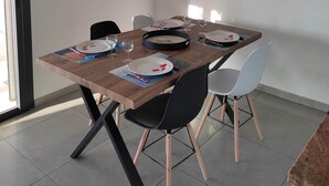Een eetgedeelte met een houten tafel, zwarte stoelen, een gele hanglamp en een gekaderd abstract schilderij aan de muur.