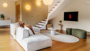 En moderne stue med en hvid sofa, trappe, fladskærms-tv og trægulv.