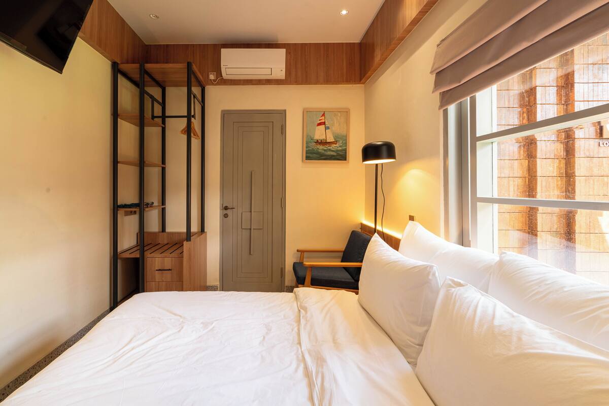 Een hotelkamer met een bed, een bureau, een stoel, een raam met uitzicht, een deur en een schilderij aan de muur.
