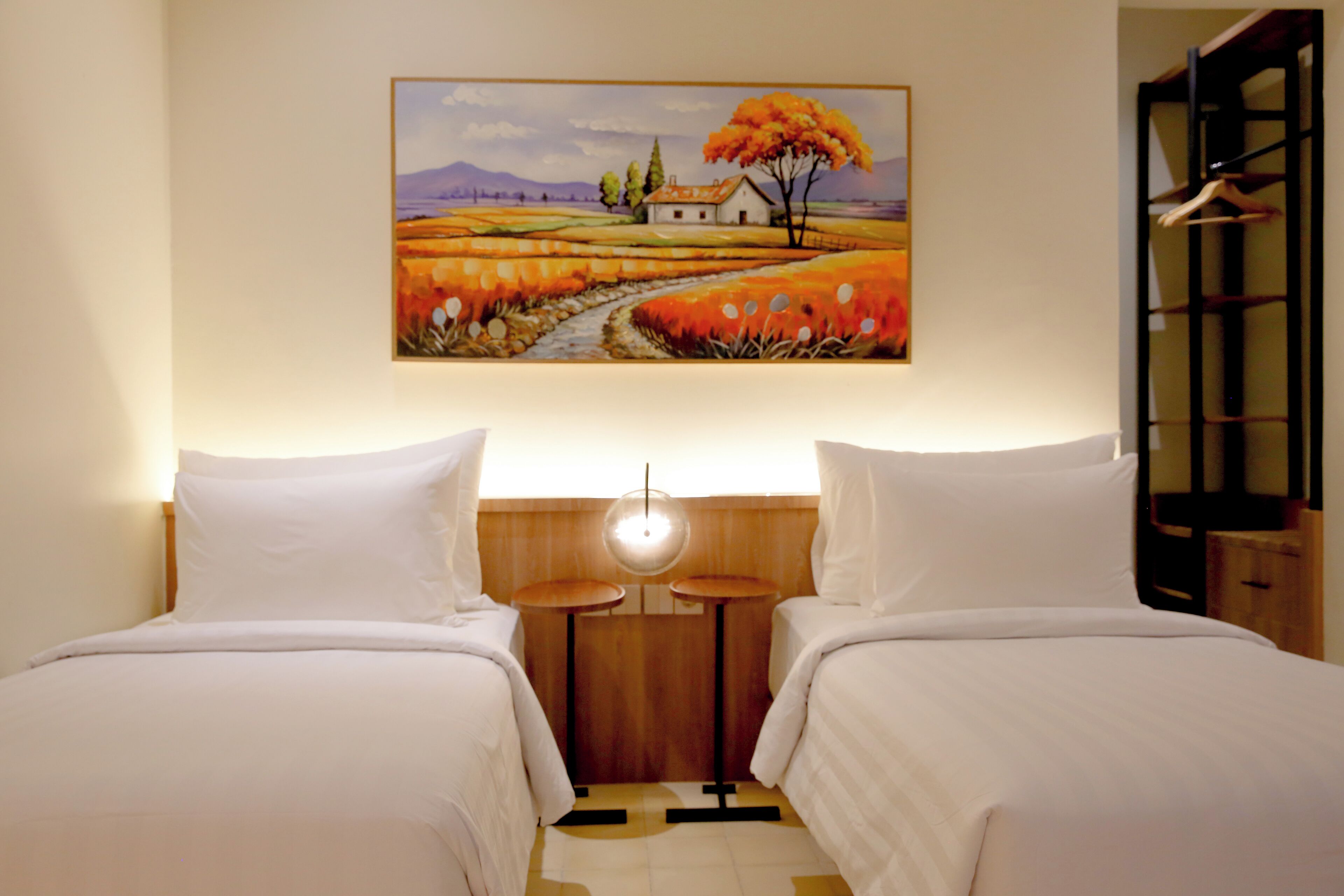 A hotel room with two beds, a painting of a landscape, and a wooden headboard.