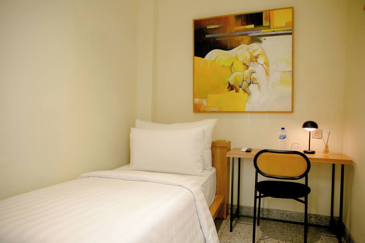 Een hotelkamer met een bed, een bureau, een stoel, een lamp en een schilderij aan de muur.