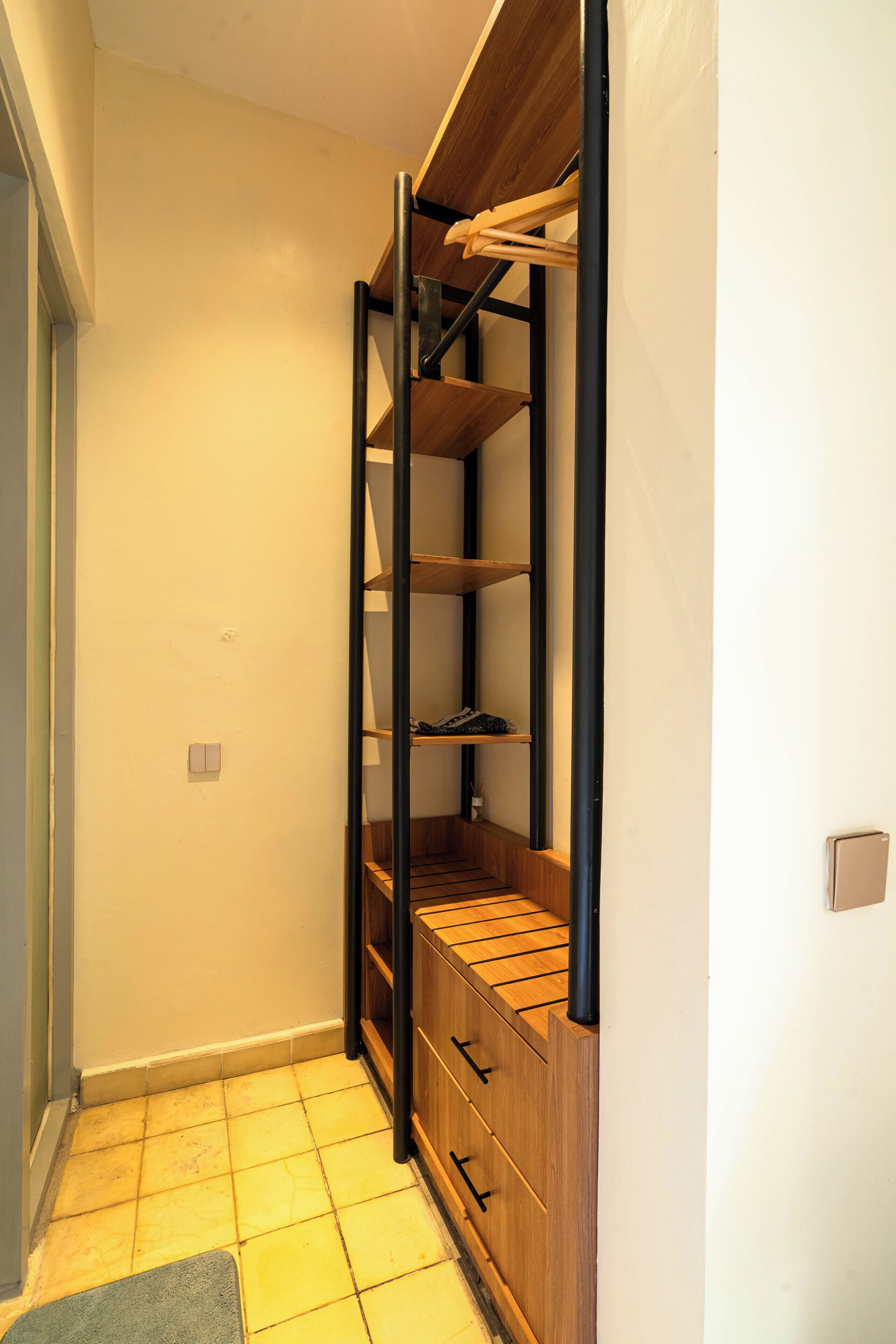 A narrow hallway with a wooden shoe rack and a black metal shelf unit against a white wall.