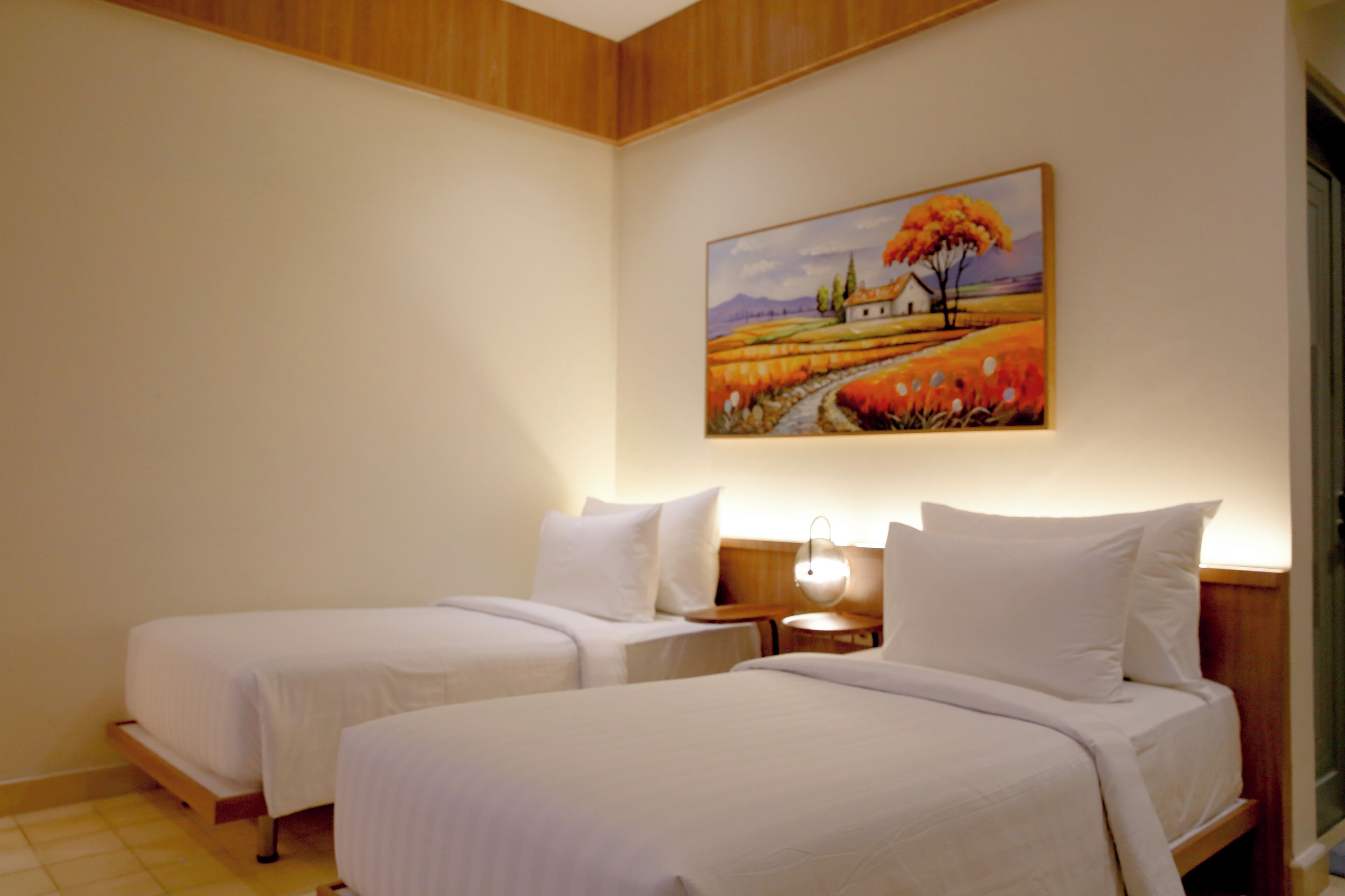 A hotel room with two beds, a painting on the wall, and a nightstand.