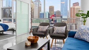 Uma sala de estar moderna com vista para a cidade, um sofá, duas poltronas, uma mesa de centro e uma planta.