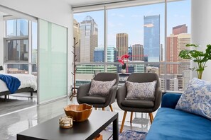 Ein modernes Wohnzimmer mit Blick auf die Stadt, inklusive Sofa, zwei Sesseln, einem Couchtisch und einer Pflanze.