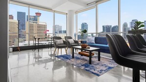 Uma sala de estar moderna com vista para a cidade, um sofá, cadeiras, uma mesa de centro e um abajur.