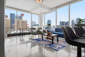 Ein modernes Wohnzimmer mit Stadtblick, einer Couch, Sesseln, einem Couchtisch und einer Stehlampe.