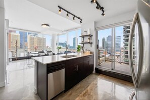 Eine moderne Küche mit einer großen Kochinsel, schwarzen Schränken und einem Edelstahl-Kühlschrank. Mehrere Fenster bieten Blick auf die Stadt.