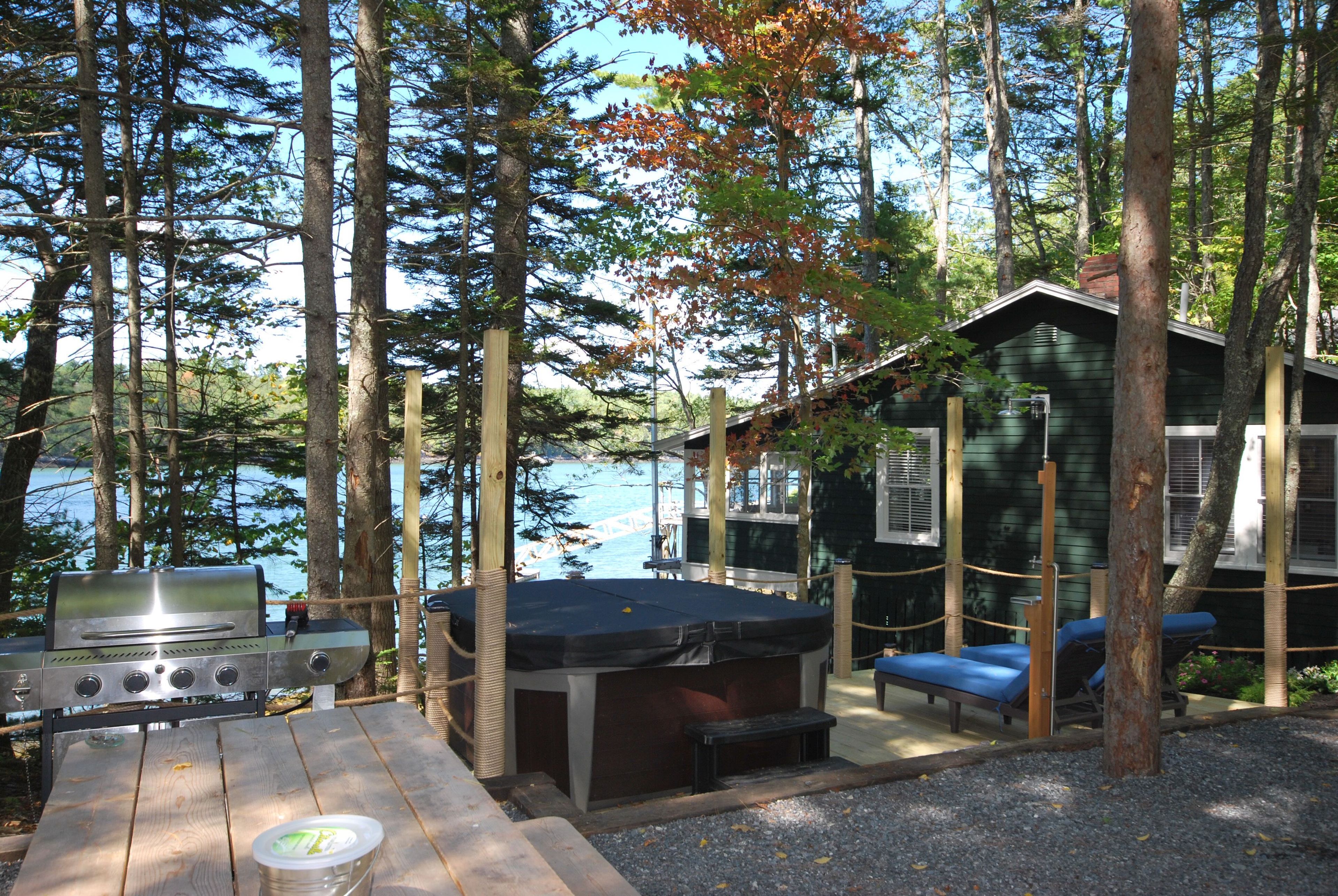 Una cabaña junto al lago con una parrilla, jacuzzi y zona de estar.