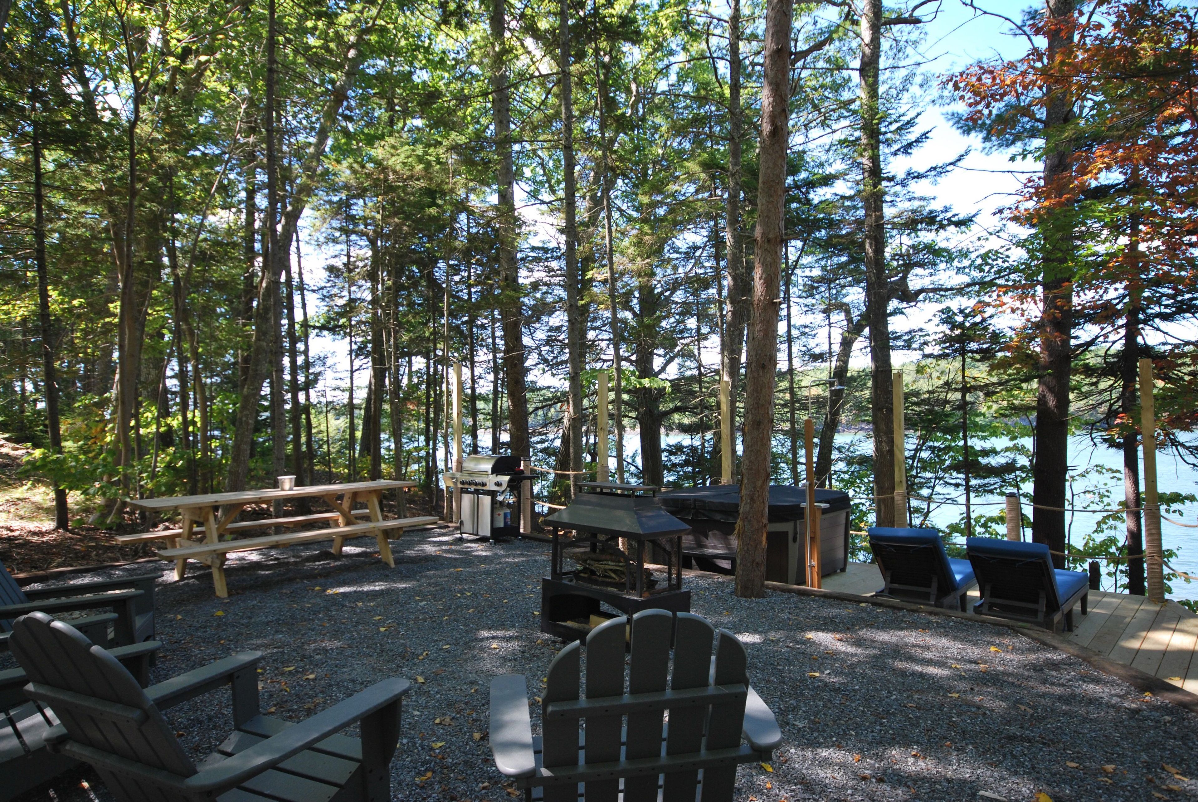 Um camping com mesas de piquenique, churrasqueira e cadeiras Adirondack.