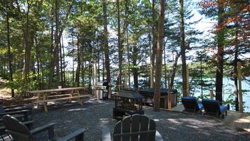 Um camping com mesas de piquenique, churrasqueira e cadeiras Adirondack.
