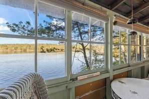 Una habitación con ventanas amplias, una mesa redonda y vistas a un cuerpo de agua y árboles.
