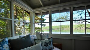 A room with a large window overlooking a lake, a bed with multiple pillows, and a view of trees.