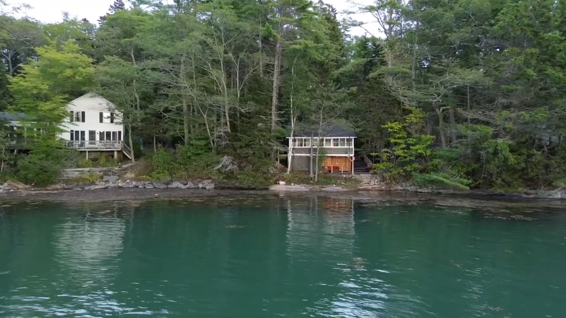 A lakeside property with two buildings, one larger with a balcony and the other smaller with a porch.