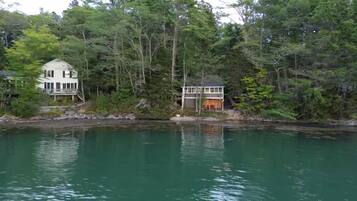 A lakeside property with two buildings, one larger with a balcony and the other smaller with a porch.