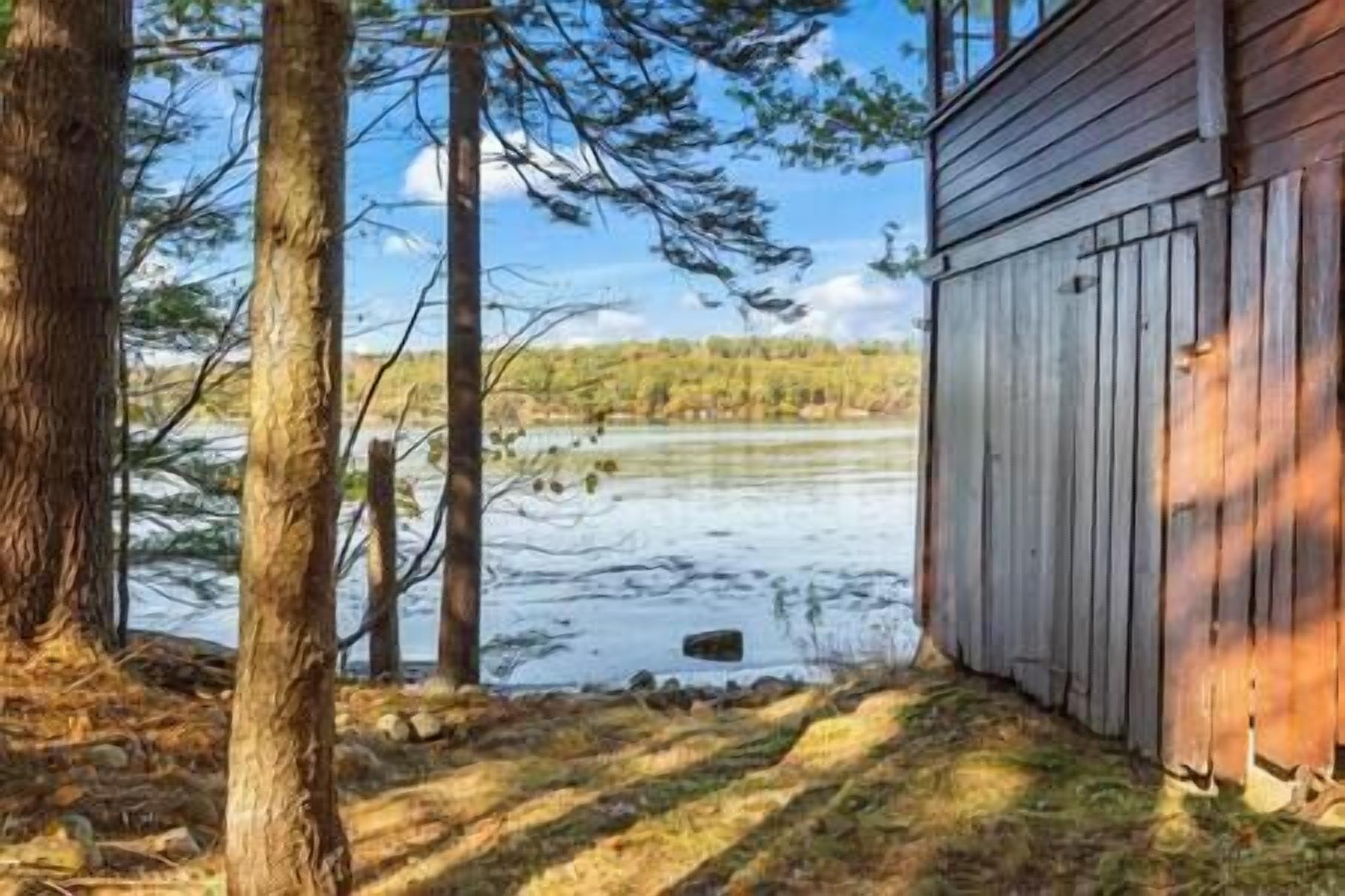 Un bâtiment en bois doté d’un toit en pente, entouré d’arbres et bordé par une étendue d’eau.