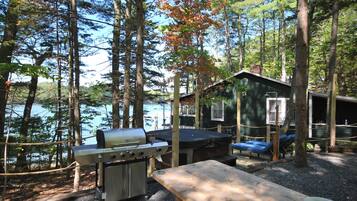 Cabana à beira do lago, com churrasqueira e mesa de piquenique.