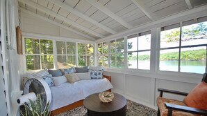 A room with a large window, a bed, a fan, a round table, and a chair.