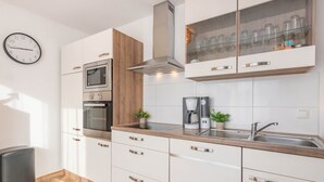 Una cocina moderna con armarios blancos, un lavamanos de acero inoxidable, horno empotrado y cafetera.