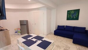 A compact living space with a dining table, a sofa, a refrigerator, and a door. - Prince Apartment (Napoli)