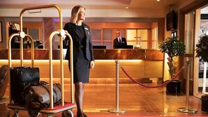 Ein Hotel-Empfangsbereich mit Empfangstresen, rotem Teppich, Gepäckwagen und einer Absperrschlange.