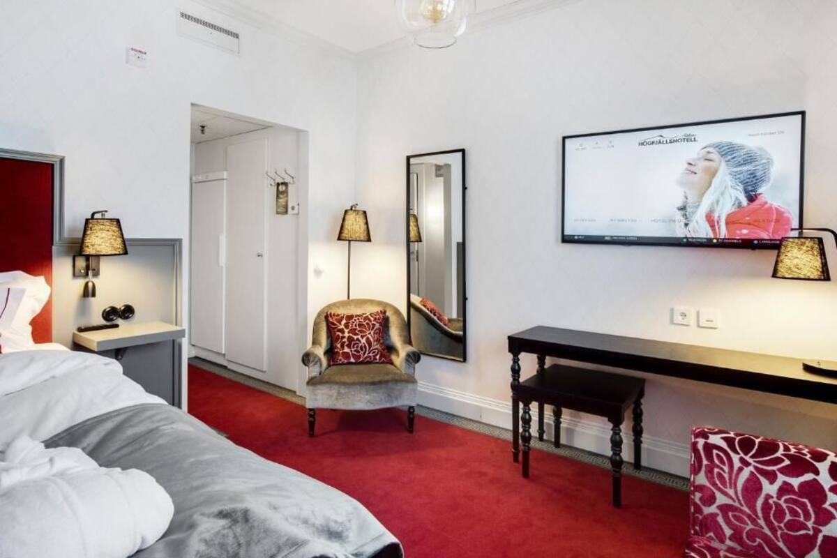 Een hotelkamer met een bed, bureau, stoel, televisie en spiegel.