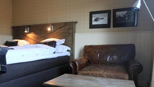 Ein Hotelzimmer mit einem Bett, einem Ledersessel, einem Holztisch und zwei gerahmten Bildern an der Wand.