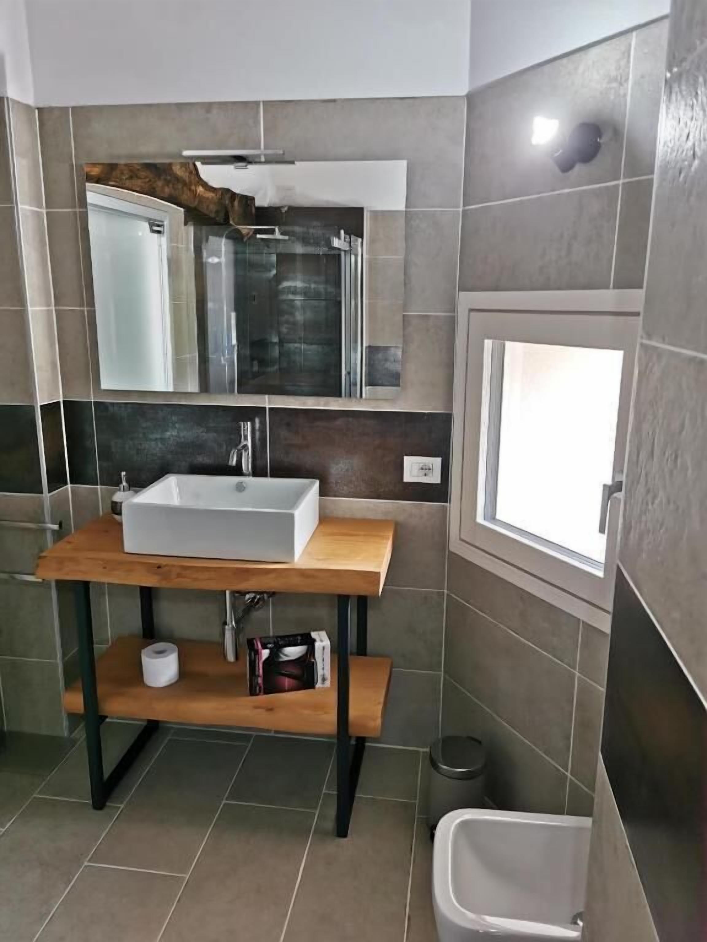 A bathroom with a wooden vanity, a large mirror, a white sink, and a small window.