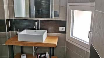 Un baño con tocador de madera, un espejo grande, un lavabo blanco y un ventanal pequeño.