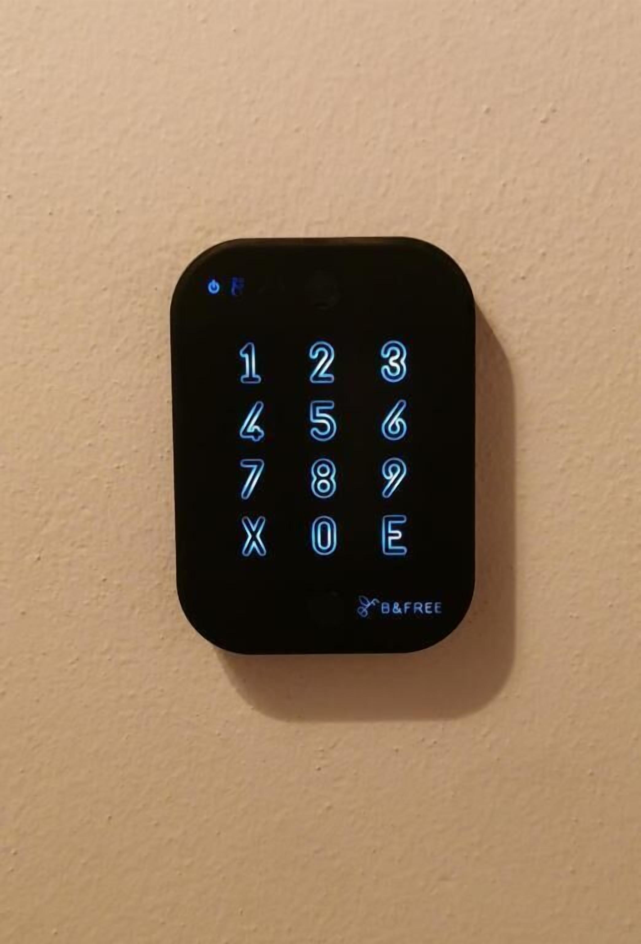 Een zwart numeriek keypad met verlichte cijfers en het B&FREE logo.