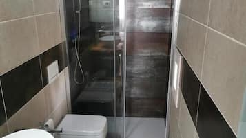 A bathroom with a shower enclosure, a toilet, and a sink.