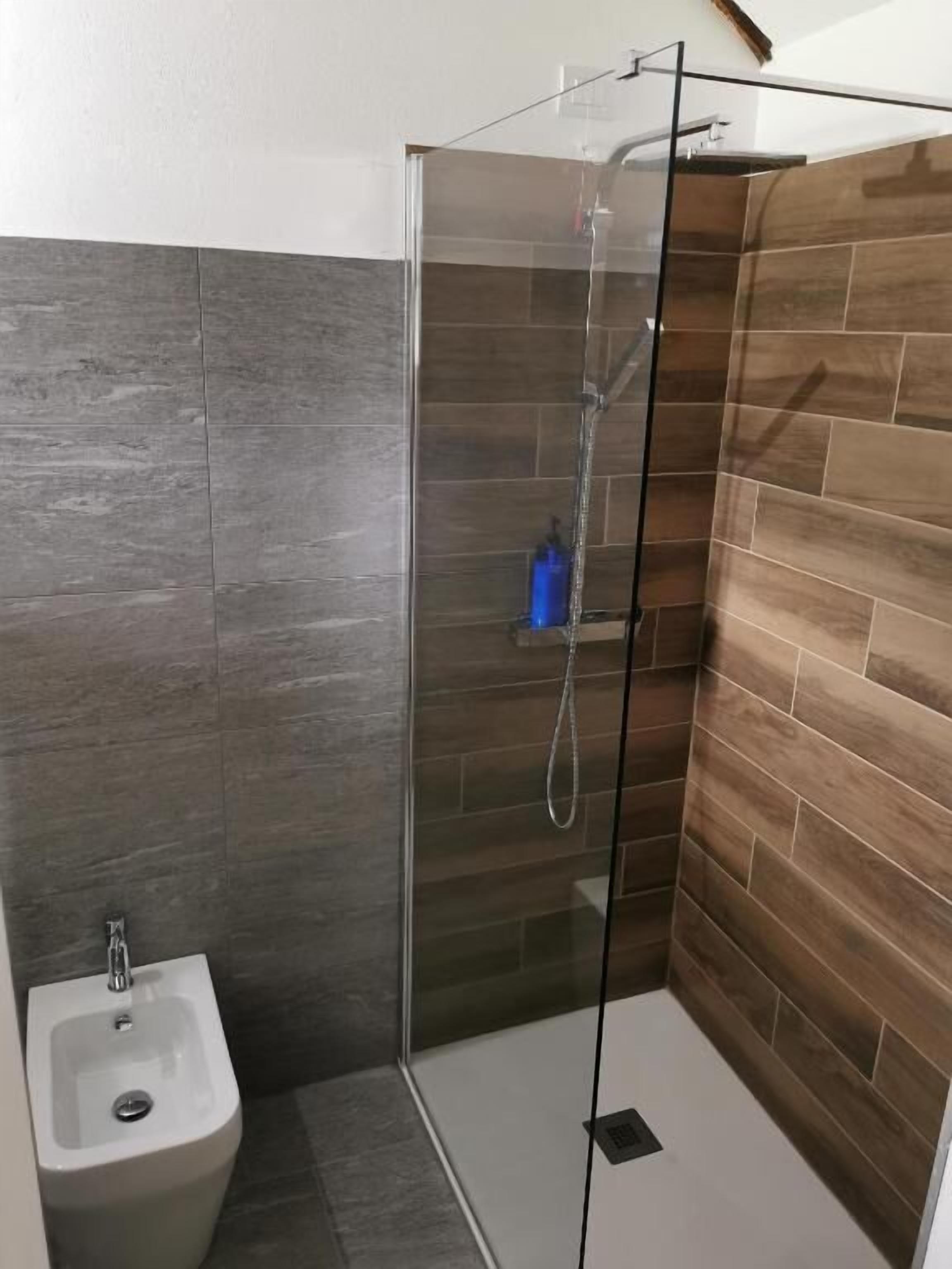 Ducha con puerta de cristal, bidé y revestimiento de madera en las paredes.