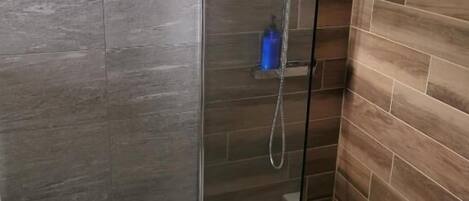 Ducha con puerta de cristal, bidé y revestimiento de madera en las paredes.