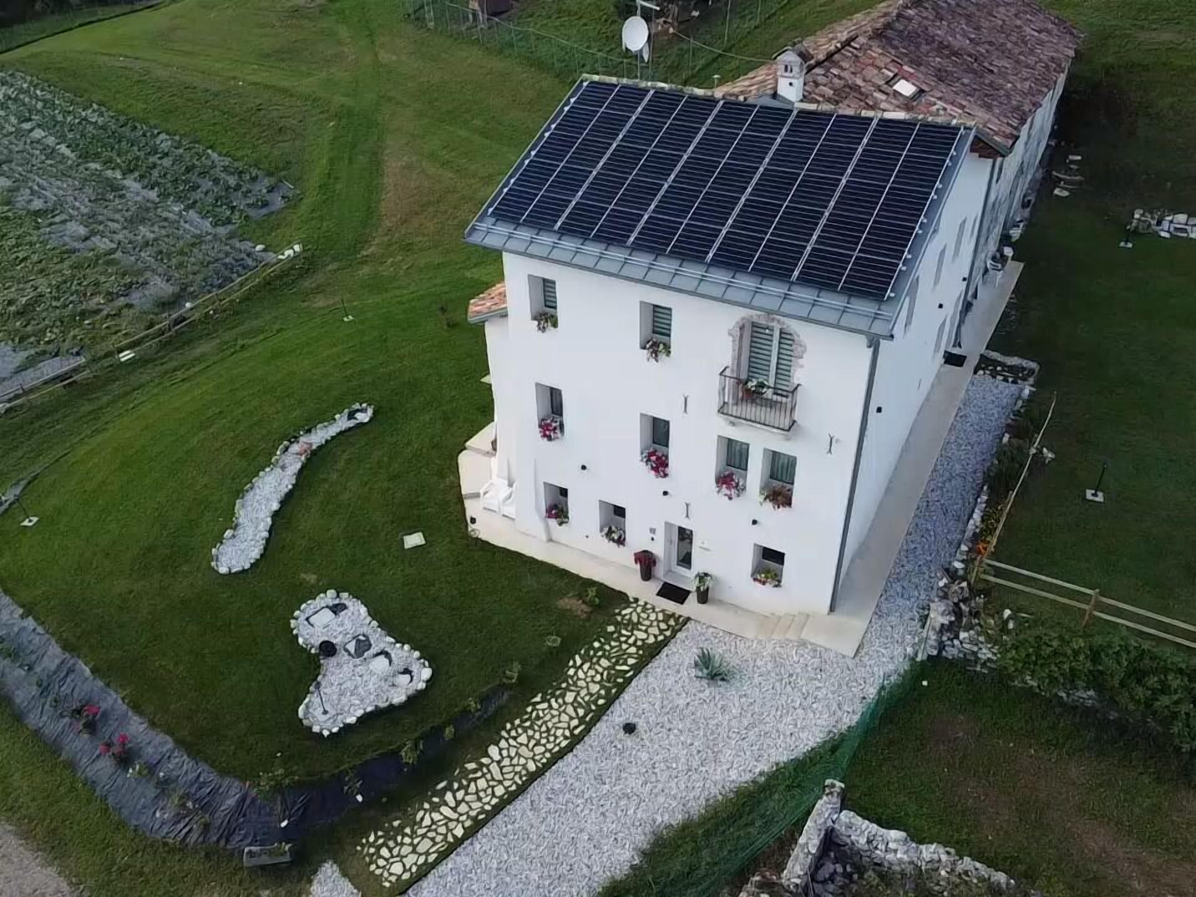 A white building with a solar panel roof, surrounded by a well-maintained lawn and stone pathways.