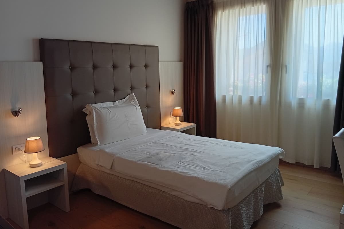 Un dormitorio con una cama grande, dos mesitas de noche, una lámpara de pared y una ventana con cortinas.