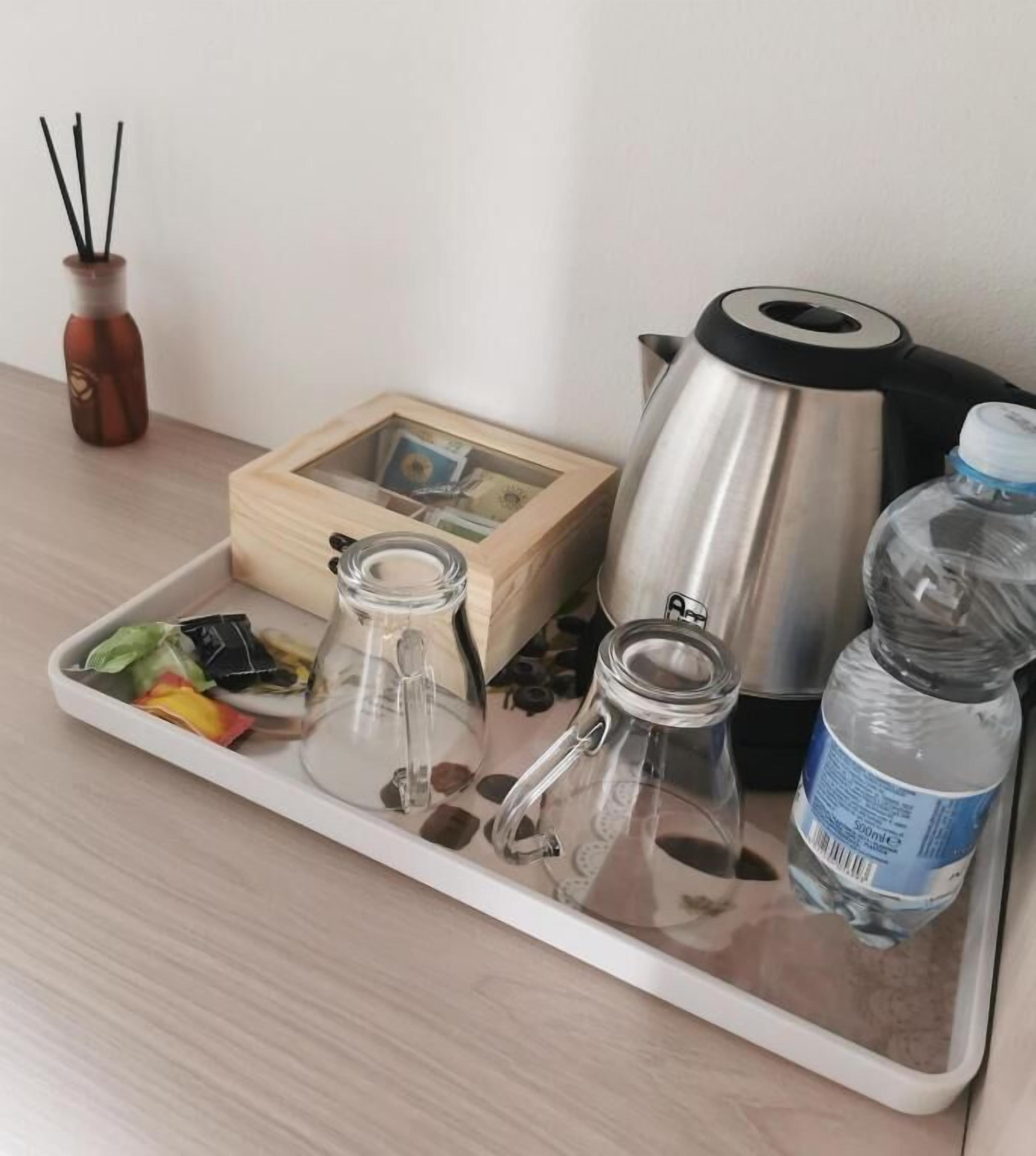 A tray with a glass jar, a metal pot, a bottle, and a wooden box on a wooden surface.