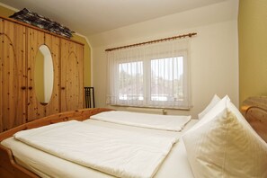 A room with two beds, a wooden wardrobe, a window with sheer curtains, and a radiator. - Cozy vacation apartment near the water - Ferienhaus Stark vacation apartment 02 (Ralswiek)