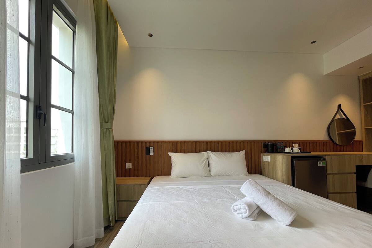 A hotel room with a bed, a desk, a mirror, and a window with curtains.