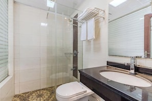 Un baño con ducha envuelta en vidrio, inodoro blanco, lavabo negro y espejo con toallero.