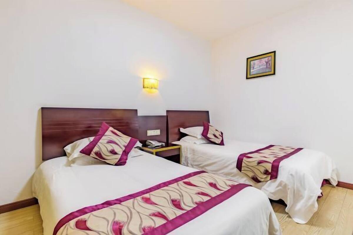 A hotel room with two beds, a nightstand, a wall-mounted light, and a framed picture.