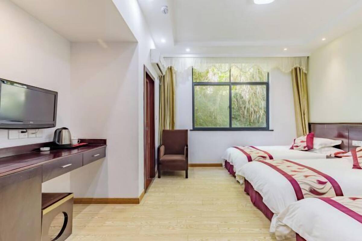 A hotel room with a TV, a desk with a kettle, a chair, two beds, and a window with curtains.