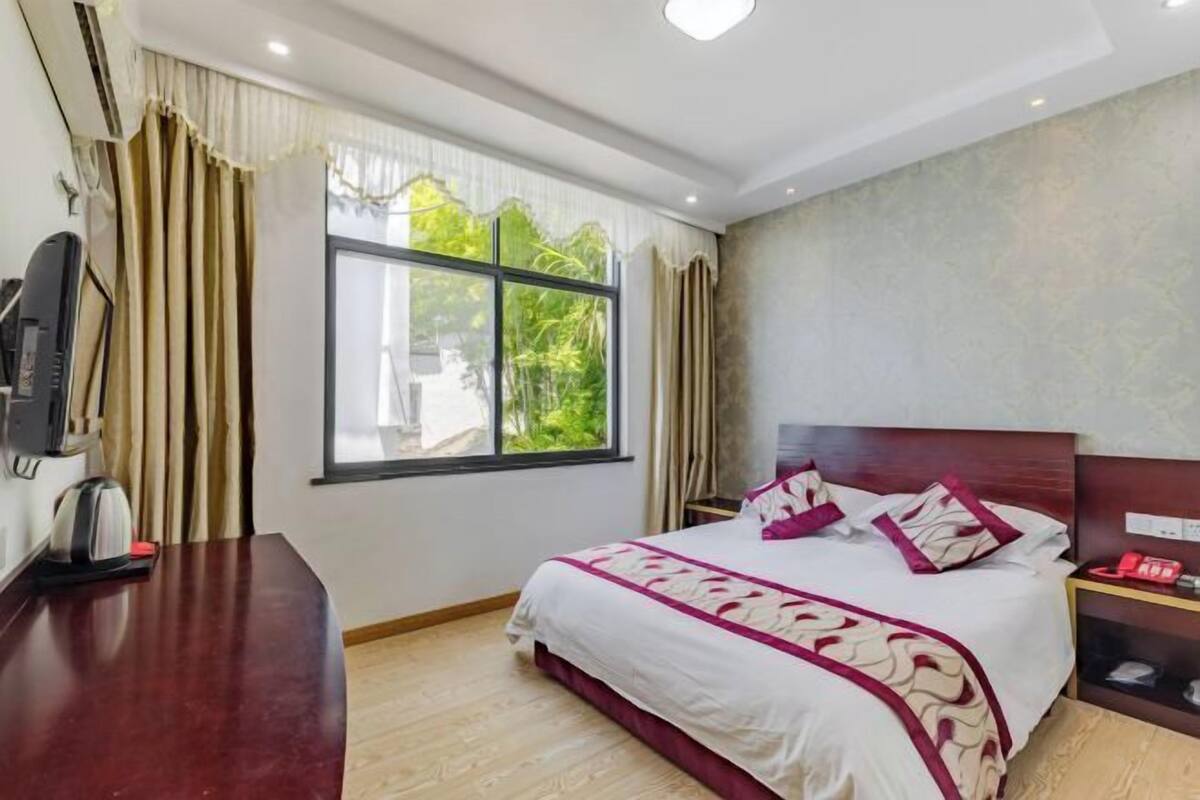 A hotel room with a bed, a desk, a telephone, and a window with curtains.